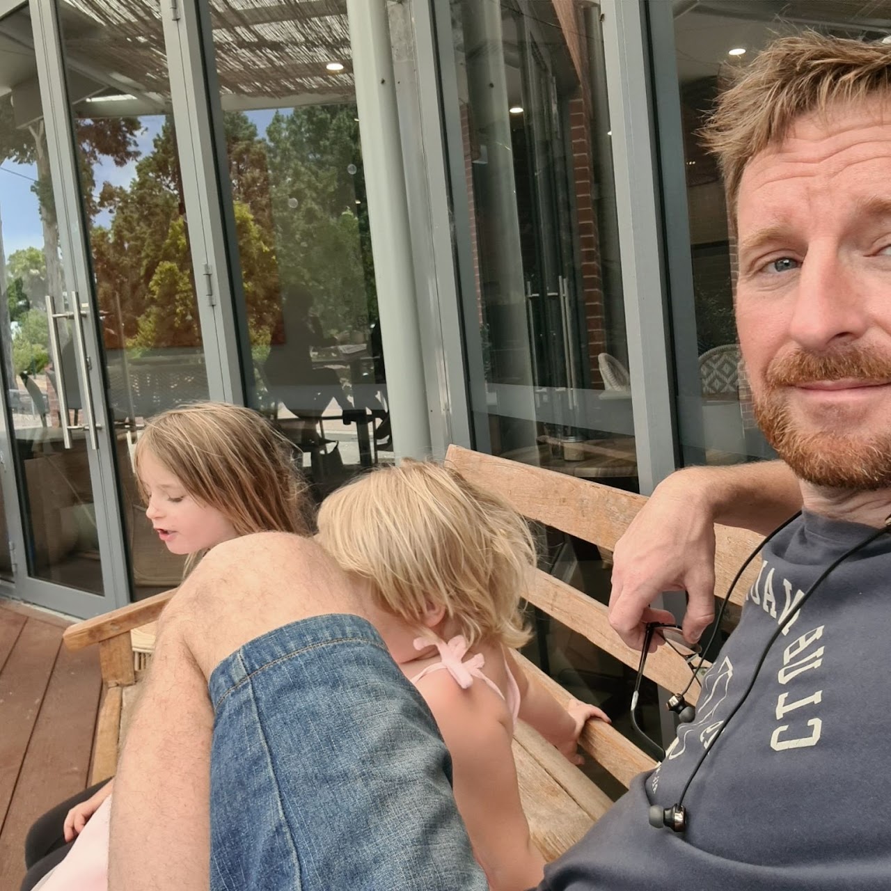 Andrew sitting on a bench with his two young daughters on a sunny afternoon